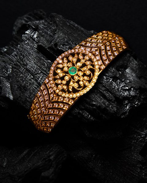 Wide cz kada with round floral medallion and emerald centre. Photographed at the shop.