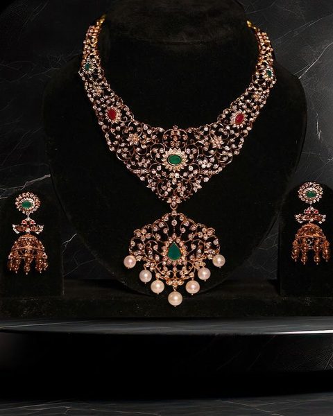CZ bridal necklace with emerald green centre, red accents, pearl drop pendant and jhumkas. Photographed at the shop.