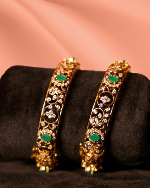 Pair of gold openwork bangles with white stones and green oval stones on velvet roll. Photographed at the shop.