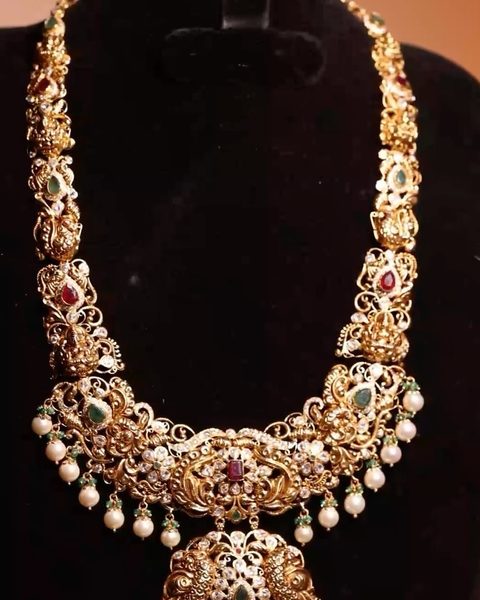 Long nakshi haram with lakshmi links, peacock pendant, small white stones and pearl drops. Photographed at the shop.