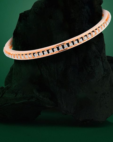 Thin rose gold bangle with a single row of white stones on charcoal rock. Photographed at the shop.