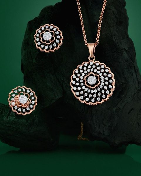 Rose gold diamond sunburst pendant on chain with matching stud earrings on charcoal rock. Photographed at the shop.