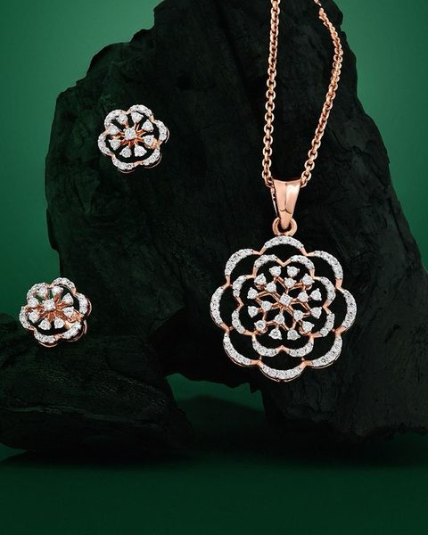Rose gold diamond flower pendant on chain with matching studs on black rock. Photographed at the shop.
