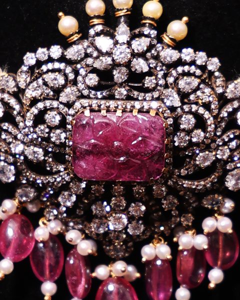 Macro of carved pink stone centrepiece with CZ scrolls, pearl crown, ruby bead drops. Photographed at the shop.