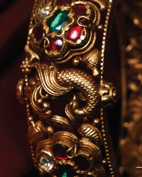 Close up of antique gold kada with peacock motif, ruby, emerald and white stones. Photographed at the shop.