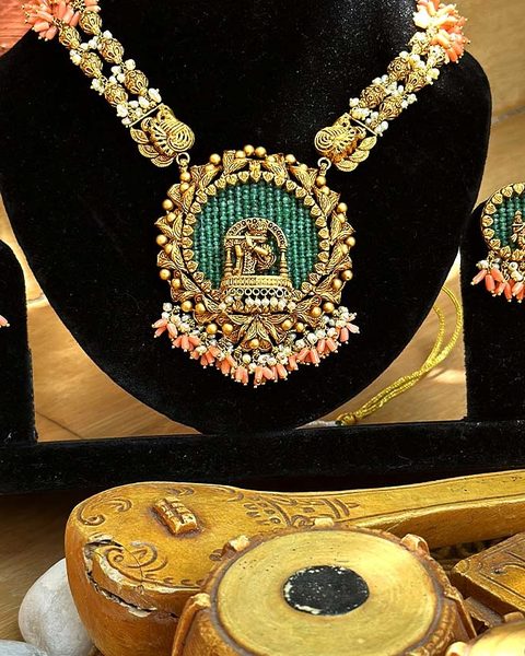 Necklace with round Krishna pendant on green bead ground, coral tassels, matching earrings. Photographed at the shop.