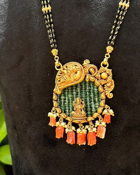 Black bead three strand chain with lakshmi pendant on emerald bead field and coral drops. Photographed at the shop.