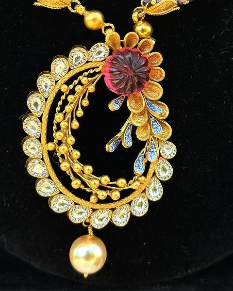 Gold pendant with polki drops, carved ruby flower, blue leaves, pearl drop on blue bead chain. Photographed at the shop.