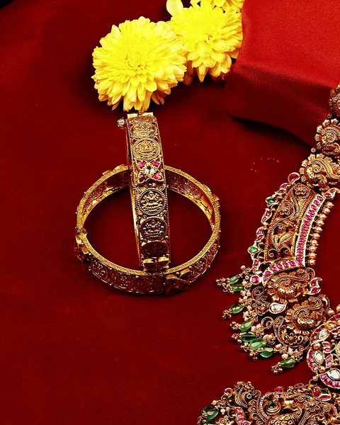 Long nakshi haram with peacock motifs and emerald drops beside two lakshmi coin bangles. Photographed at the shop.
