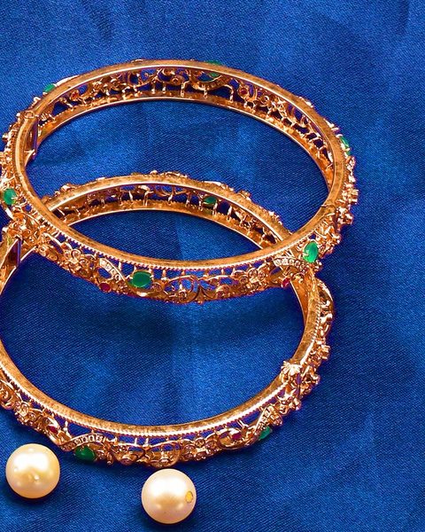 Pair of openwork gold bangles with green and red stones, loose pearls as props. Photographed at the shop.