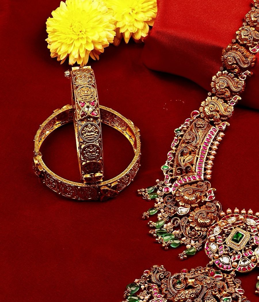 A pair of carved antique gold kadas standing on red cloth beside a long haram.
