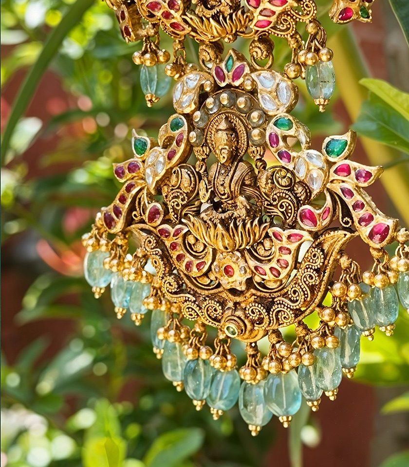 Close view of a Lakshmi pendant in antique gold with kempu rubies, uncut stones and pale green bead drops.
